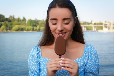 Photo of Beautiful young woman eating ice cream glazed in chocolate near river