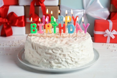 Delicious birthday cake with burning candles on table