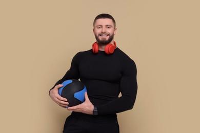 Photo of Handsome sportsman with headphones and medicine ball on brown background