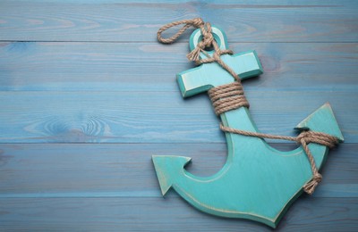 Photo of Anchor with hemp rope on light blue wooden table, top view. Space for text