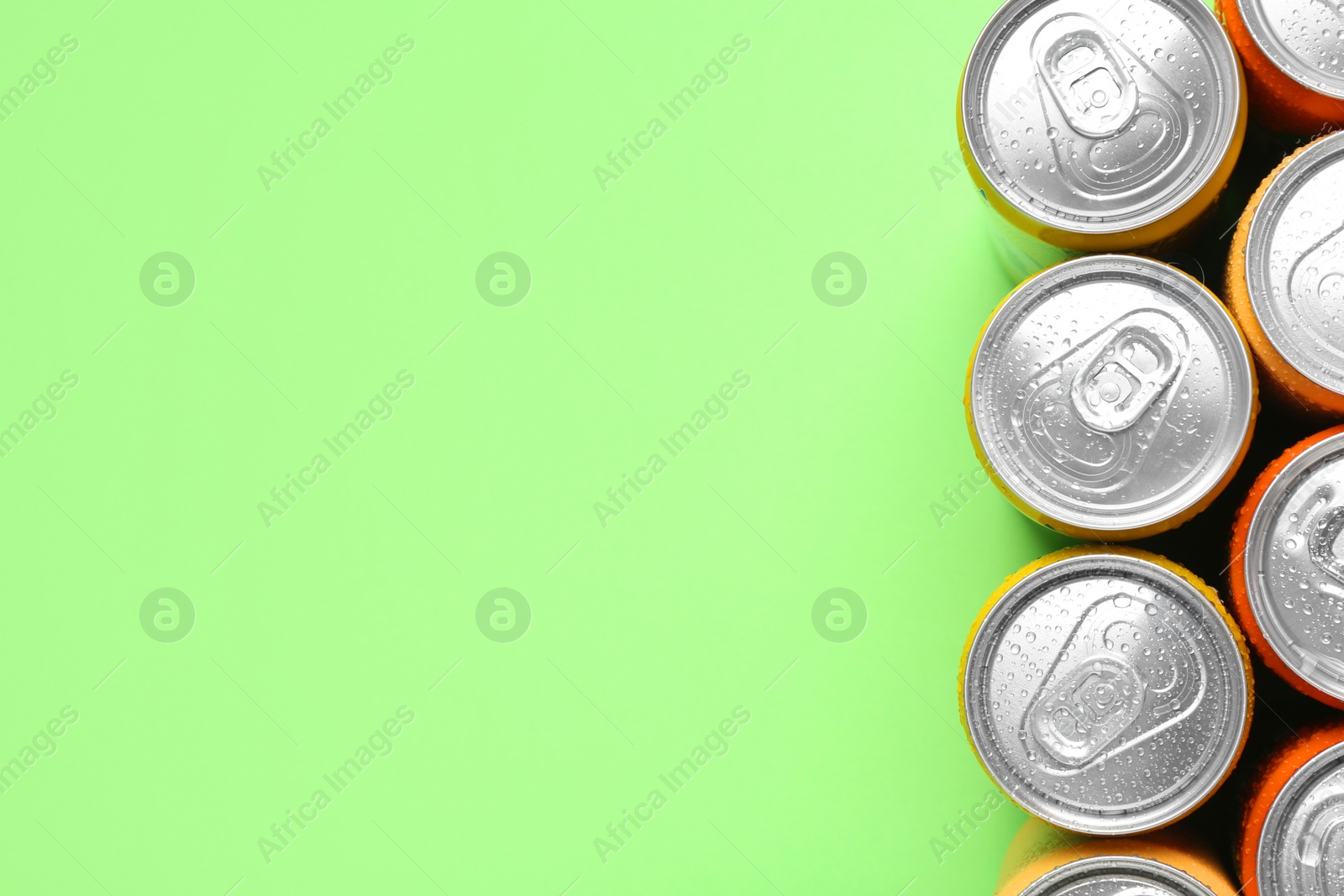 Photo of Energy drinks in wet cans on green background, top view. Space for text