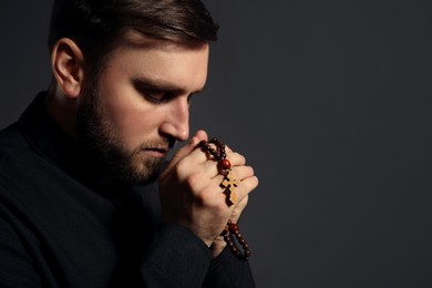 Photo of Priest with rosary beads praying on dark background. Space for text