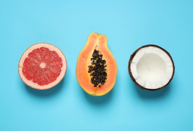 Photo of Cut ripe papaya, grapefruit and coconut on light blue background, flat lay