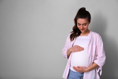 Photo of Young pregnant woman on light grey background. Space for text