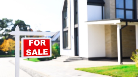 Photo of Red real estate sign near house outdoors on sunny day