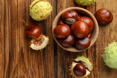 Photo of Horse chestnuts on wooden table, flat lay