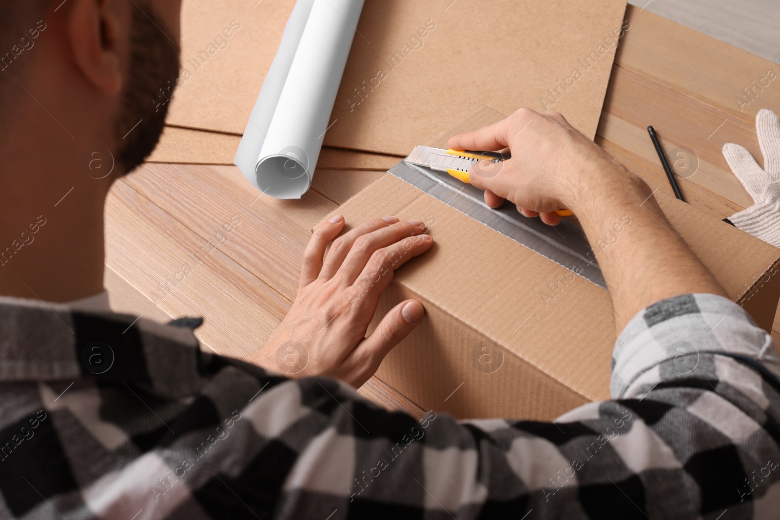 Photo of Man using utility knife to open parcel at wooden table, closeup