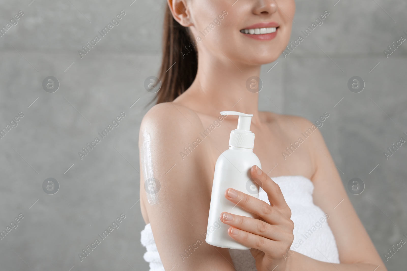 Photo of Woman with bottle of body cream near grey wall, closeup. Space for text