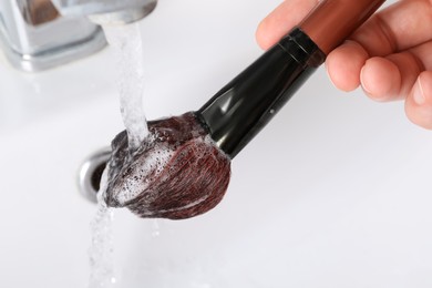 Woman washing makeup brush under stream of water in sink, closeup