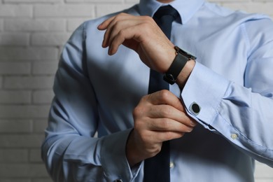 Photo of Stylish man putting on cufflink near white brick wall, closeup