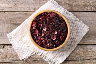 Photo of Dry hibiscus tea in bowl on wooden table, top view