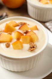 Photo of Tasty peach yogurt with granola and pieces of fruit in bowl on plate, closeup