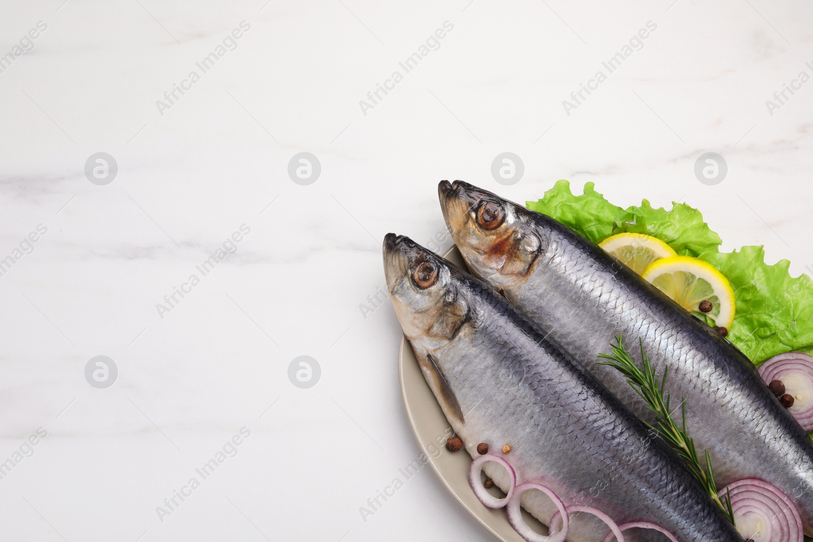 Photo of Plate with salted herrings, onion rings, slices of lemon, peppercorns and lettuce on white marble table, top view. Space for text