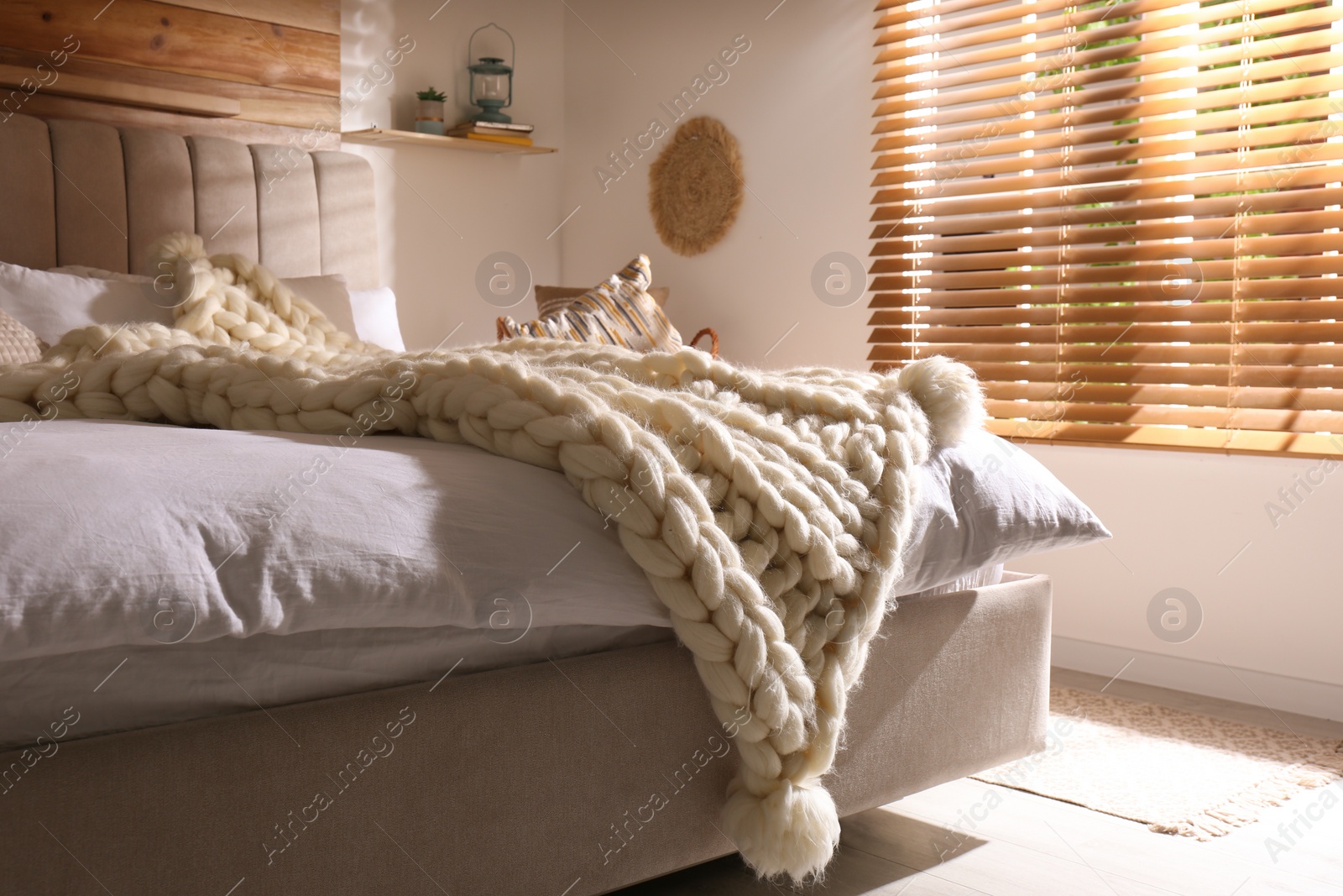 Photo of Bed with white knitted plaid indoors. Interior design