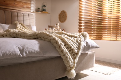 Bed with white knitted plaid indoors. Interior design