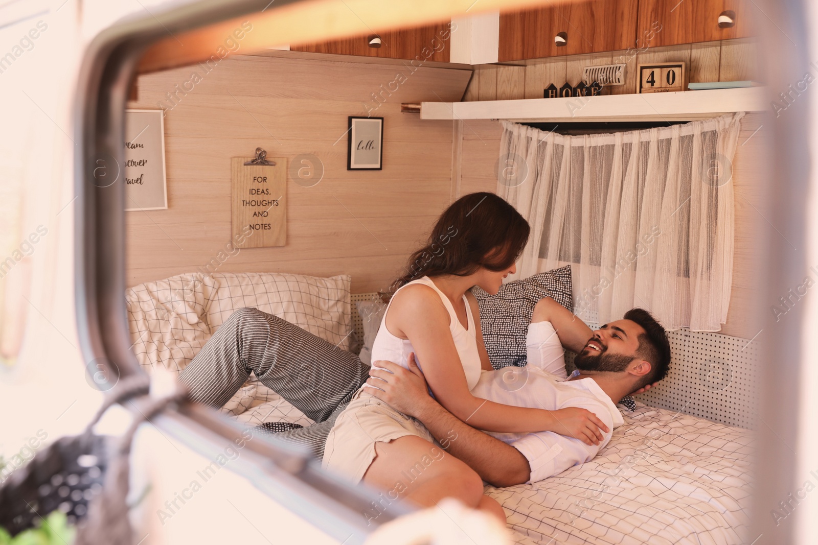 Photo of Happy young couple on bed in trailer, view from outside. Camping vacation