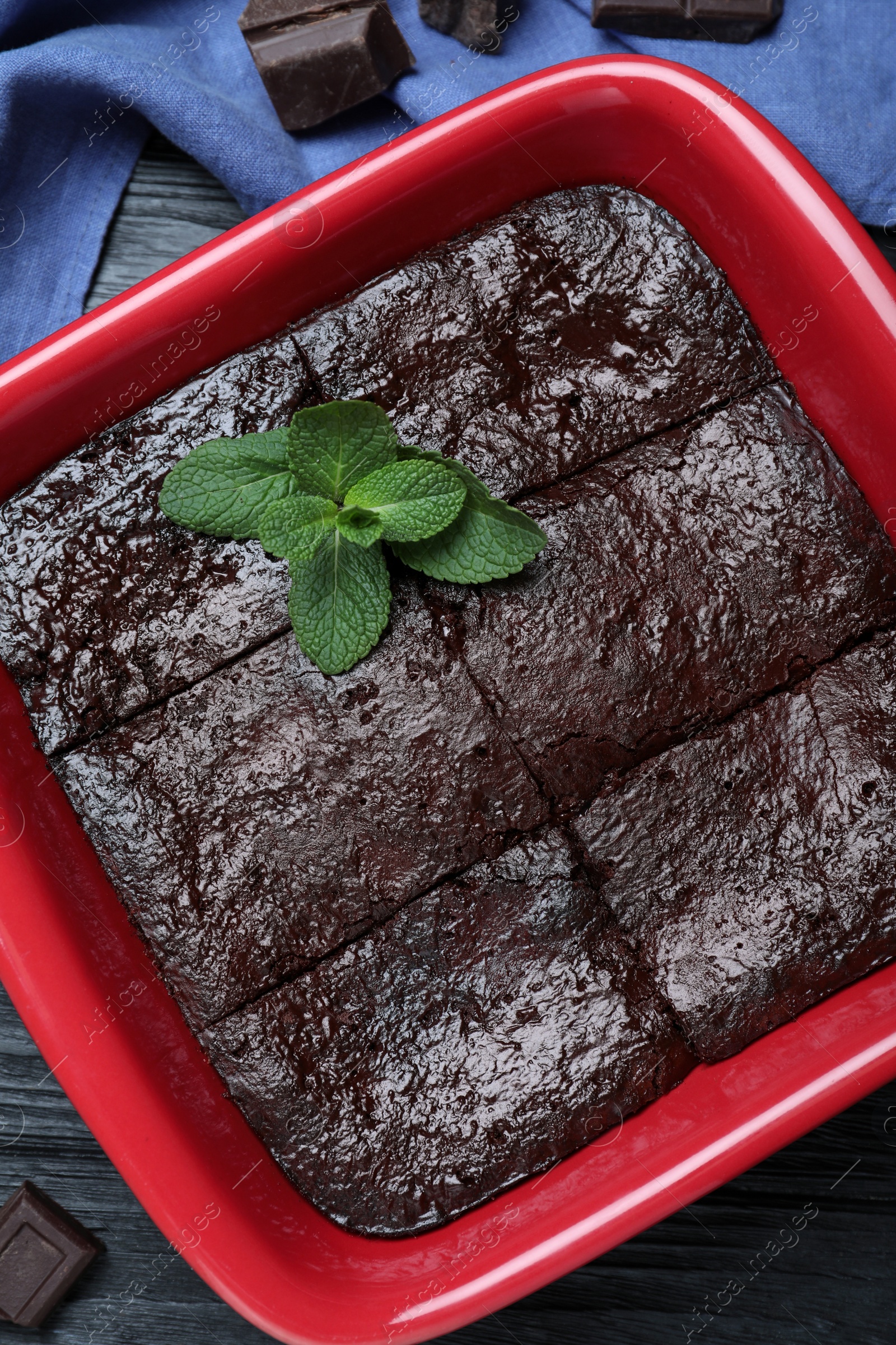 Photo of Delicious chocolate brownie with mint in baking dish on black wooden table, flat lay