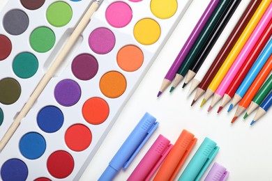 Photo of Watercolor palette, colorful pencils and markers on white background, flat lay
