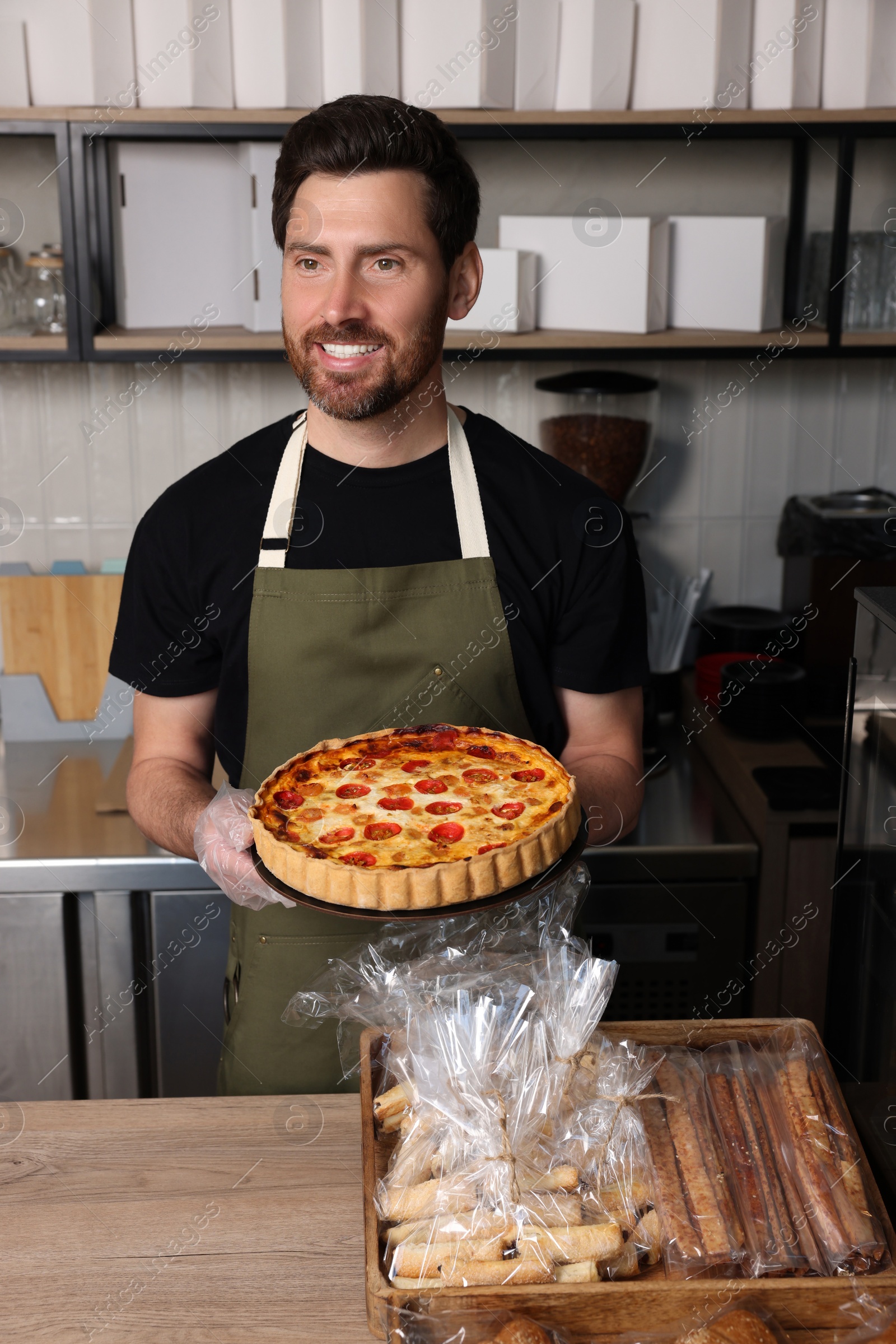 Photo of Seller with freshly baked quiche at cashier desk in bakery shop