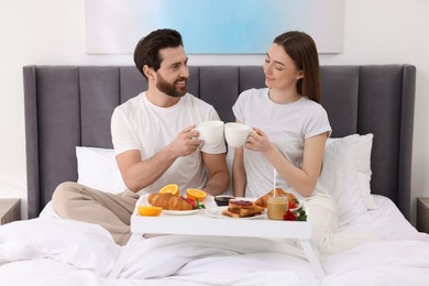 Happy couple eating tasty breakfast on bed at home