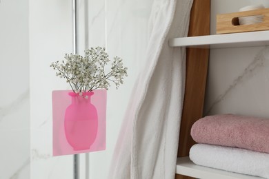 Photo of Silicone vase with flowers on shower glass panel in bathroom