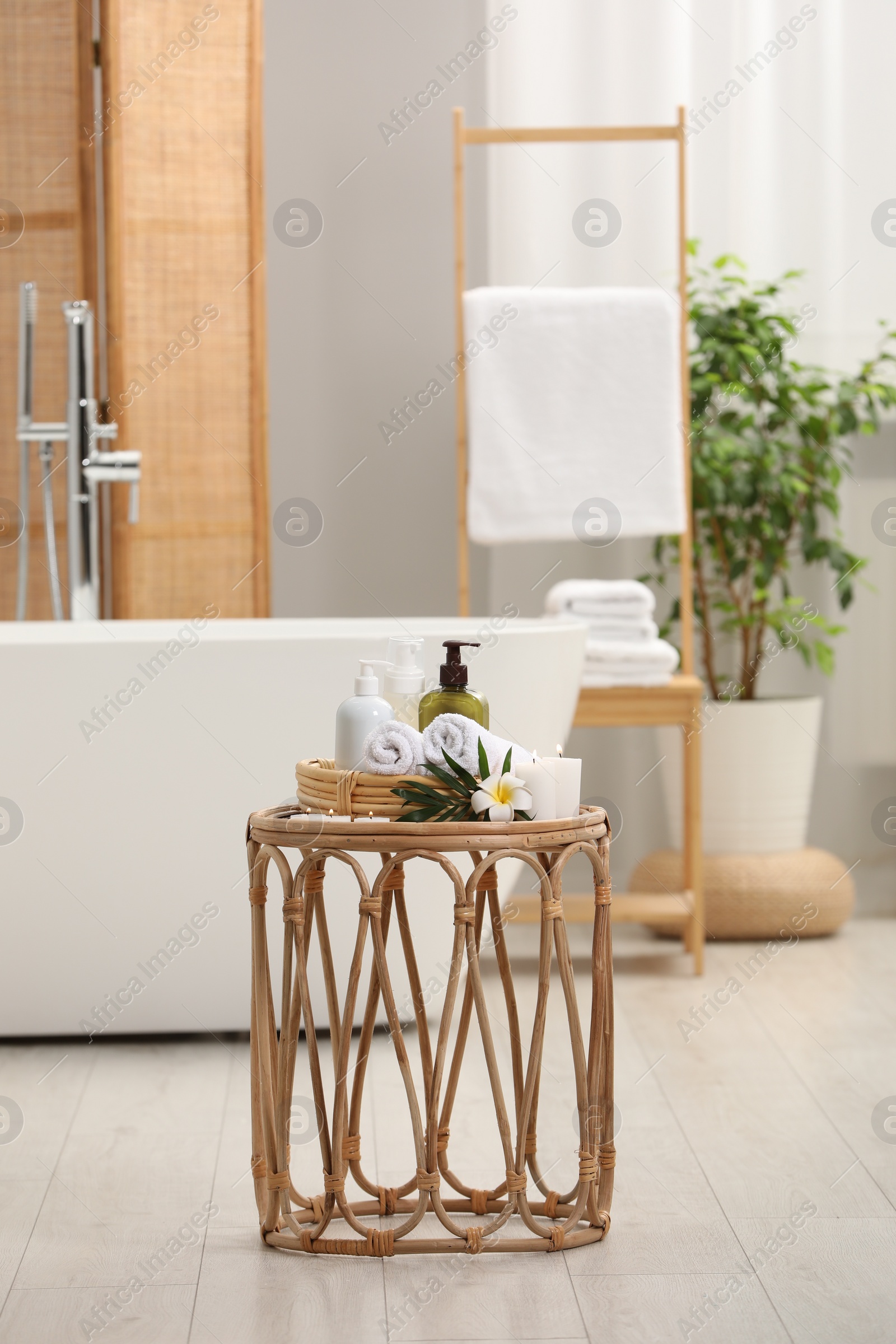 Photo of Spa products, burning candles and plumeria flower on small table in bathroom