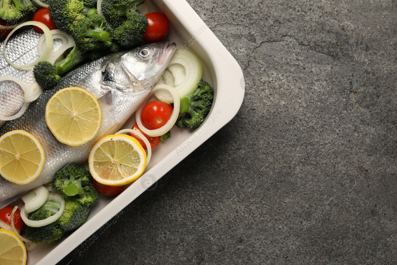 Photo of Raw fish with vegetables and lemon in baking dish on grey textured table, top view. Space for text