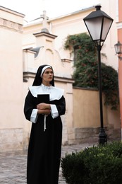Photo of Young nun with Bible on city street