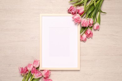 Photo of Empty photo frame and beautiful tulip flowers on wooden background, flat lay. Mockup for design