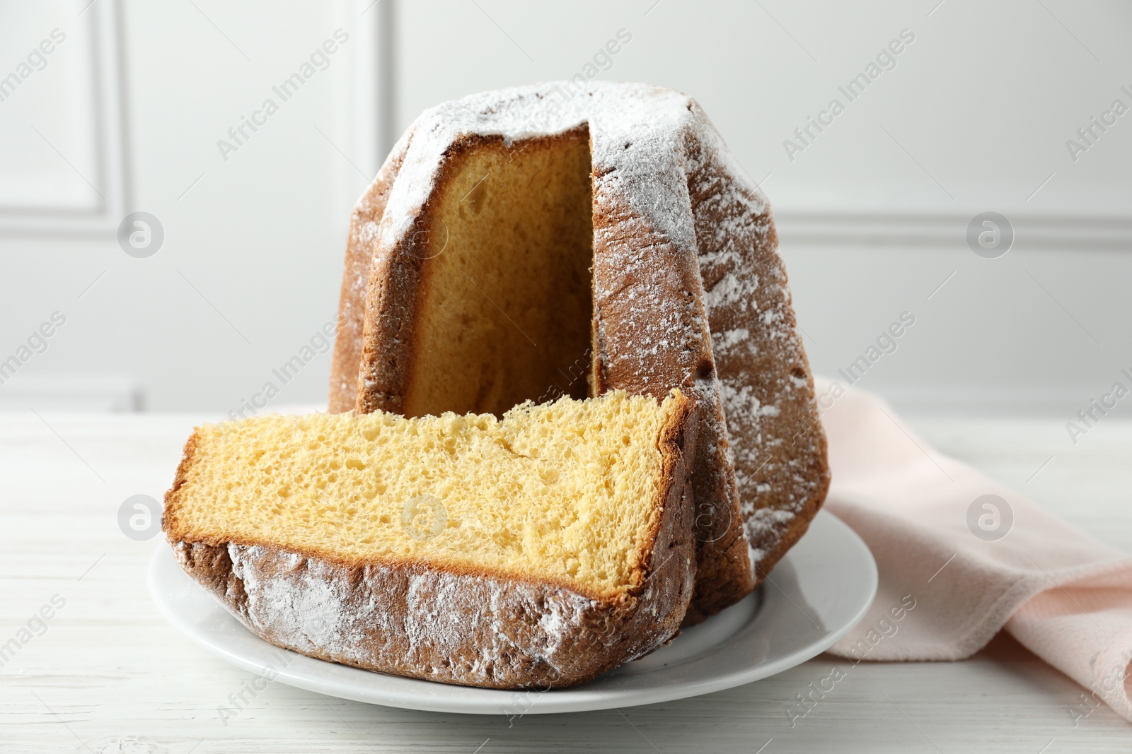 Photo of Delicious Pandoro cake decorated with powdered sugar on white wooden table. Traditional Italian pastry