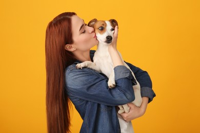Photo of Woman kissing cute Jack Russell Terrier dog on orange background