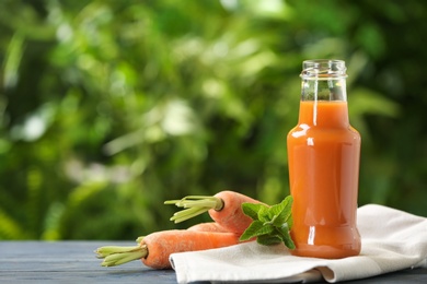 Bottle of tasty drink and carrots on table against blurred background, space for text