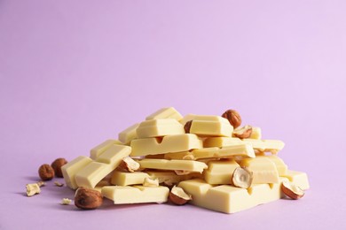 Photo of Delicious white chocolate with hazelnuts on violet background