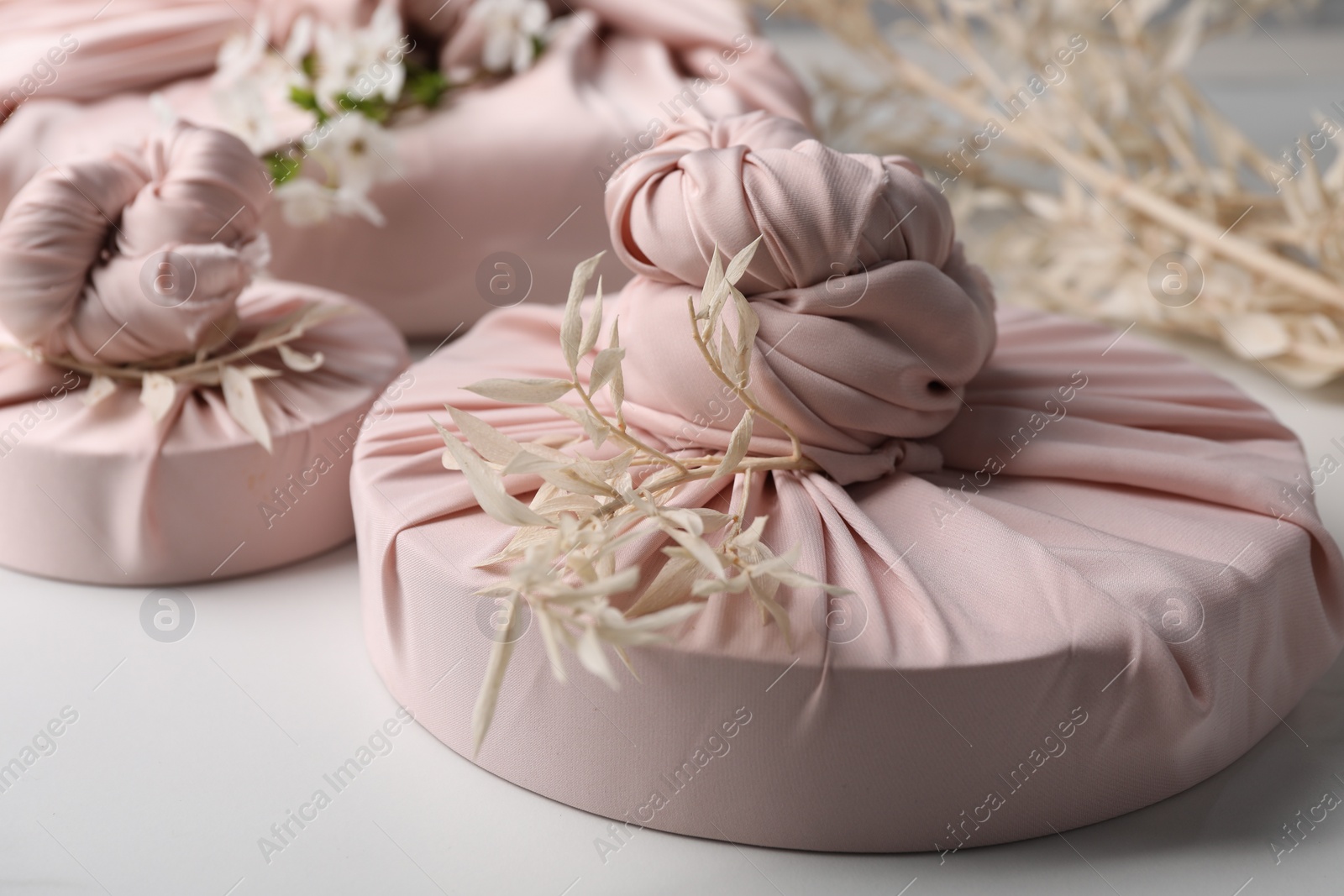 Photo of Furoshiki technique. Gifts packed in pink fabric and dried branches on white table, closeup