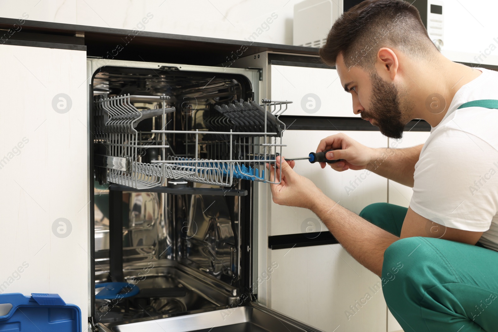 Photo of Serviceman repairing dishwasher with screwdriver in kitchen