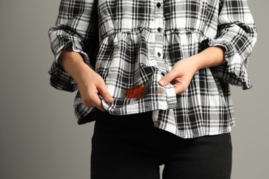 Woman showing sauce stain on her shirt against grey background, closeup