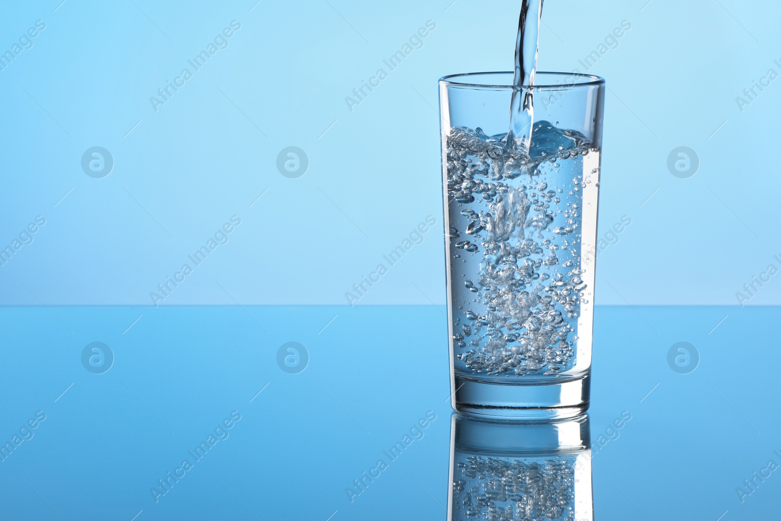 Photo of Pouring water into glass on light blue background. Space for text