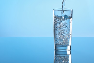 Photo of Pouring water into glass on light blue background. Space for text