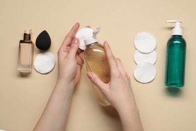 Photo of Woman using makeup remover, closeup. Cleanser, foundation, cotton pads and sponge on beige background, top view