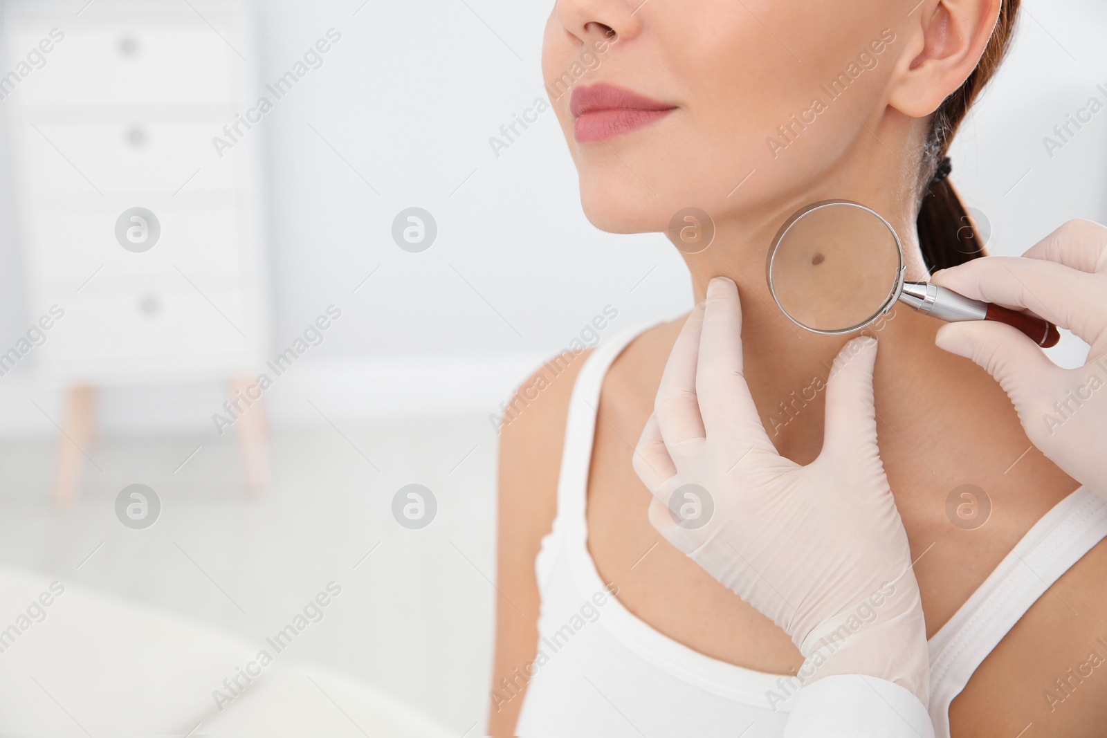 Photo of Dermatologist examining patient's birthmark with magnifying glass in clinic, closeup. Space for text