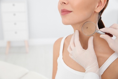 Dermatologist examining patient's birthmark with magnifying glass in clinic, closeup. Space for text