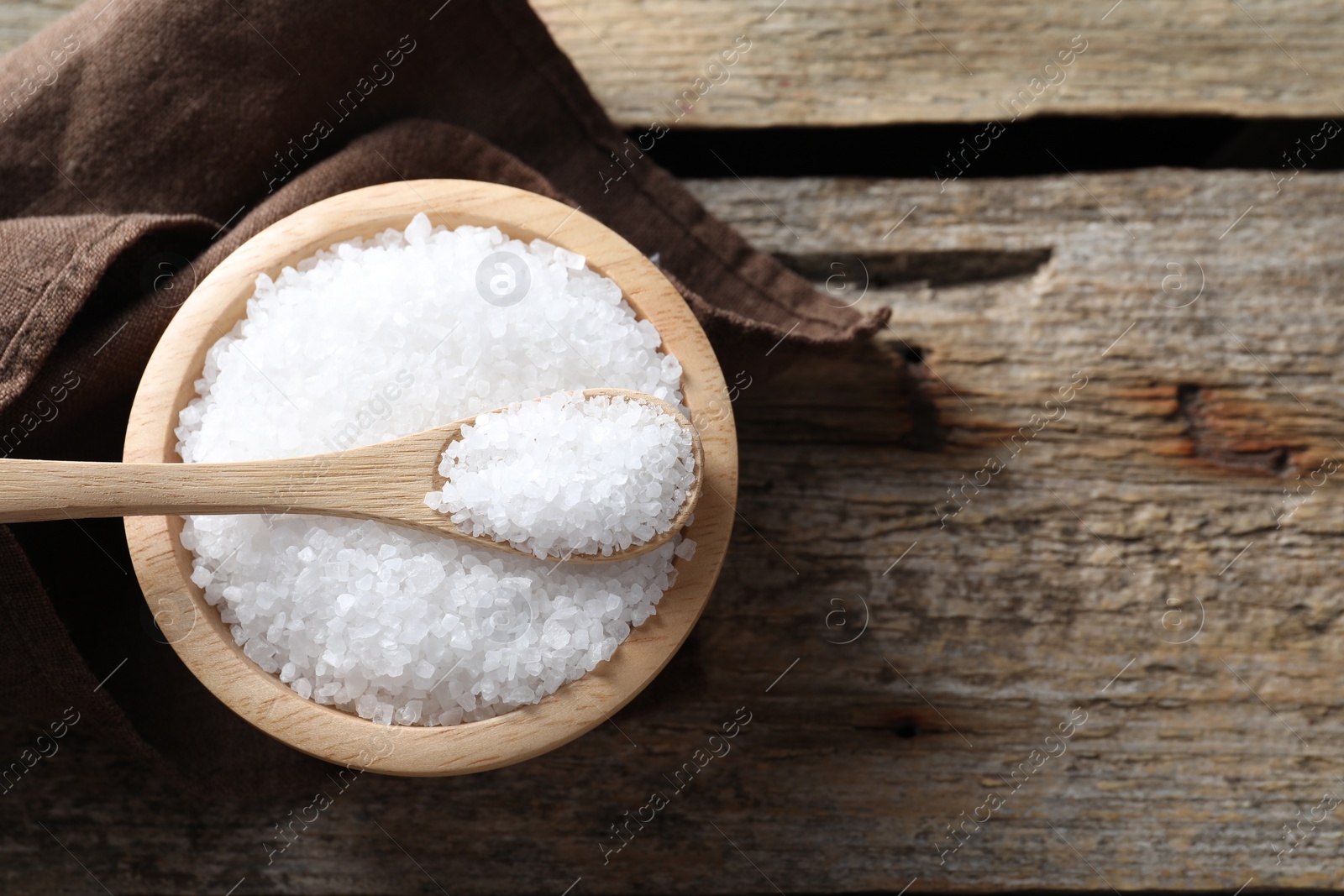 Photo of Organic salt in bowl and spoon on wooden table, top view. Space for text