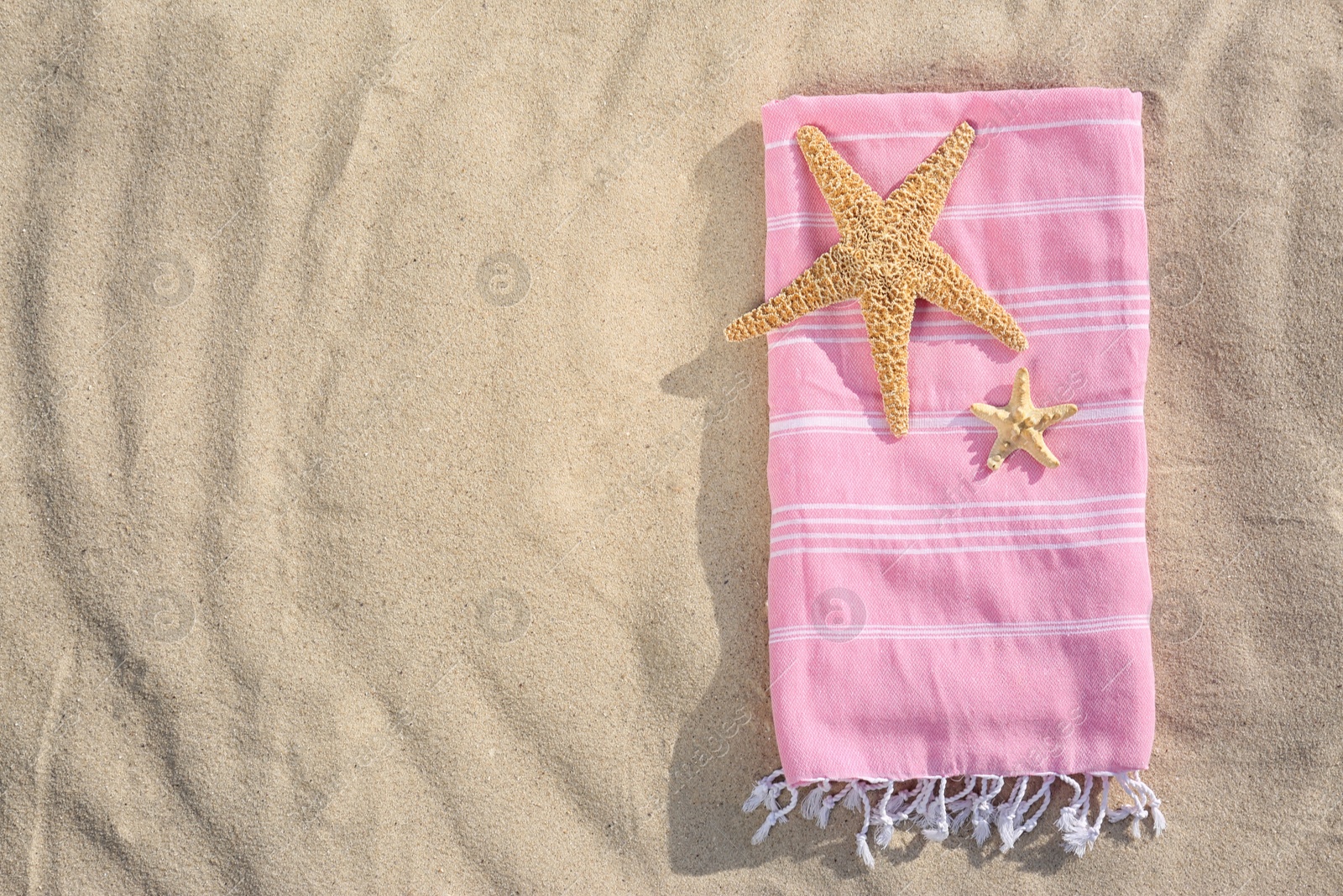 Photo of Starfishes and towel on sand, top view with space for text. Beach objects