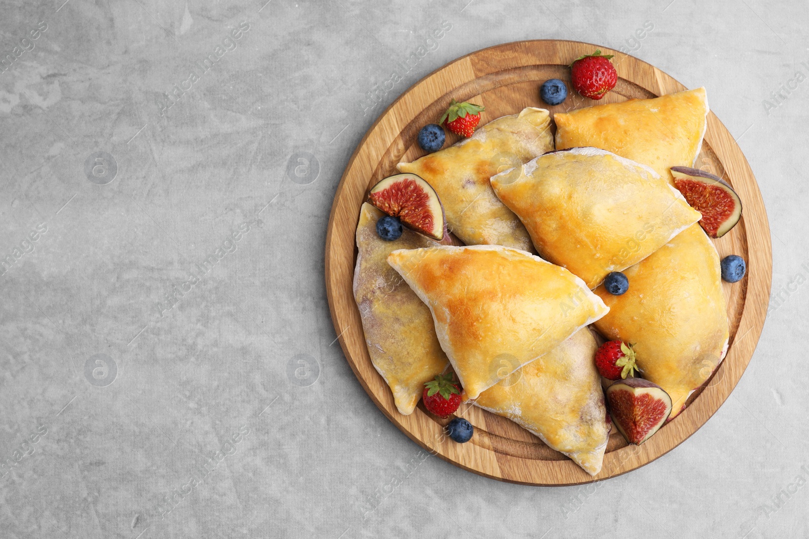 Photo of Delicious samosas with figs and berries on grey table, top view. Space for text