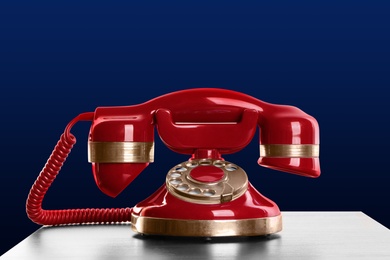 Image of Vintage red corded telephone on table against blue background