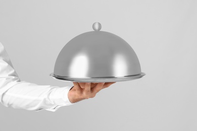 Photo of Waiter holding metal tray with lid on light background