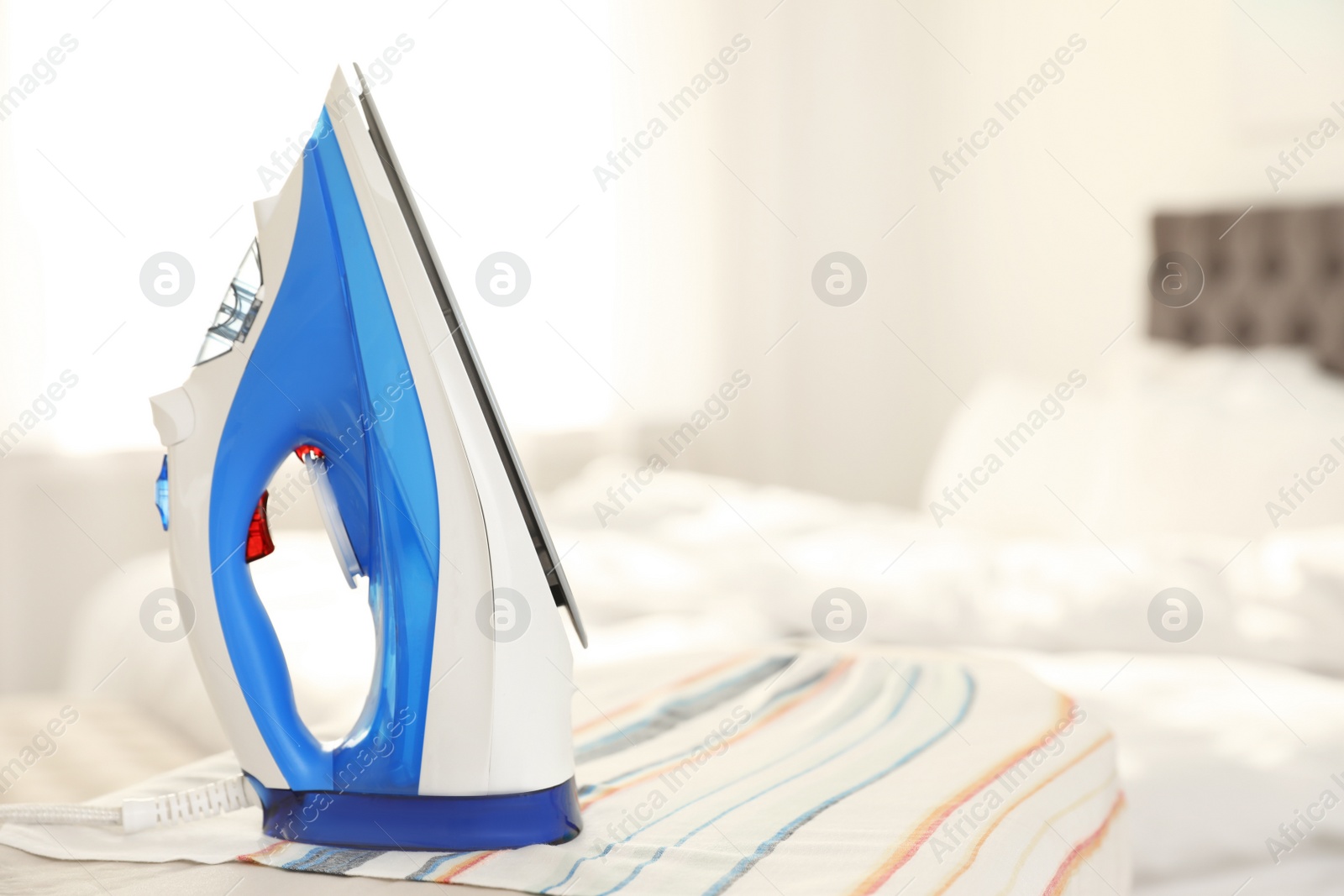 Photo of Modern electric iron on board indoors, space for text. Household appliance