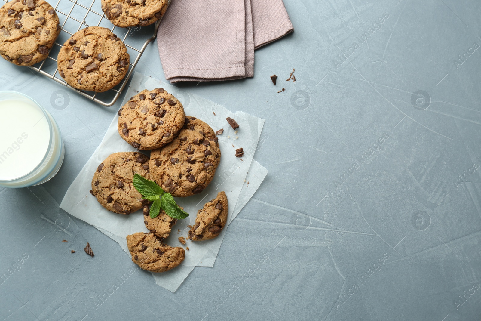 Photo of Tasty chocolate chip cookies, glass of milk and mint leaves on light grey table, flat lay. Space for text