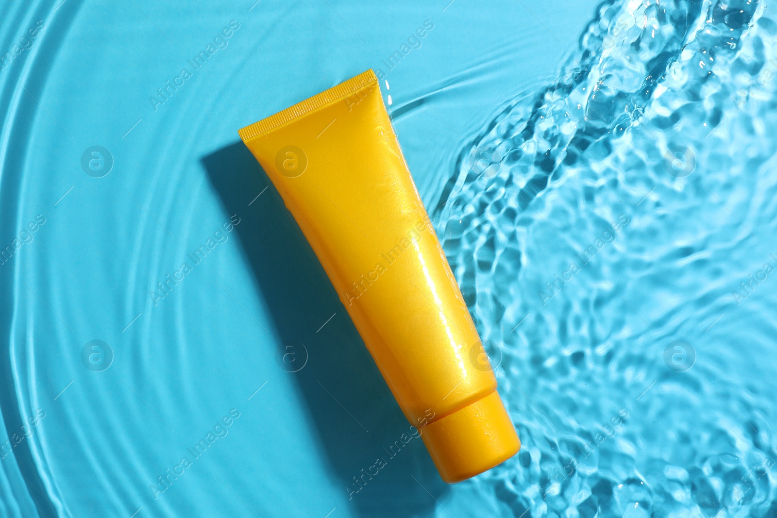 Photo of Tube with moisturizing cream in water on light blue background, top view