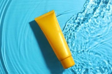 Photo of Tube with moisturizing cream in water on light blue background, top view